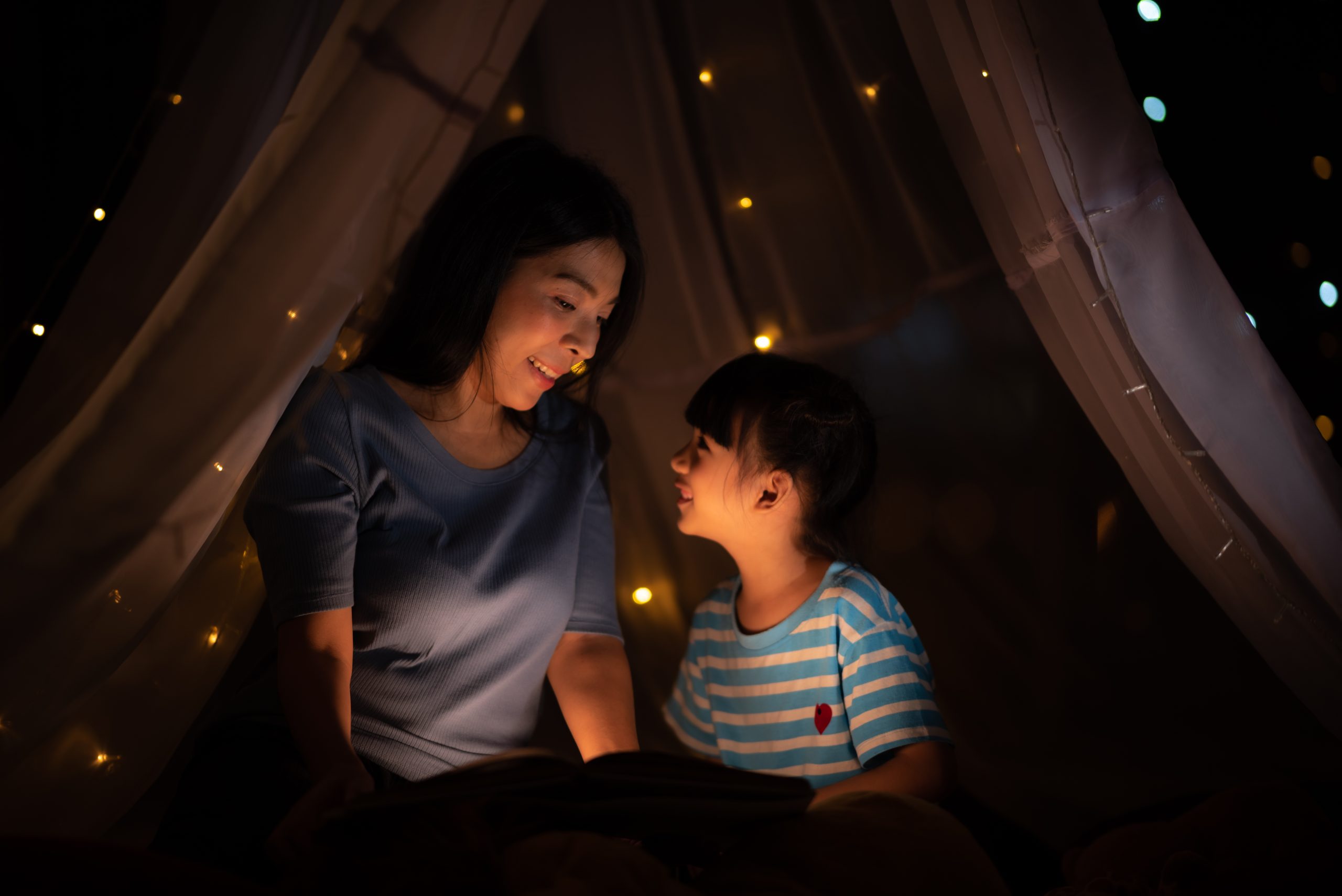 a women playing with child before sleep in children's tent. closeup happy face, lovely family concept, asian parent, smiling girl and mom, dark background.